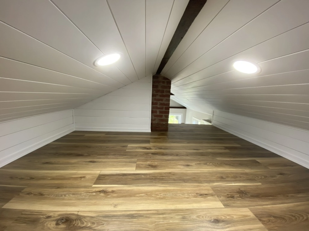 Finished attic space with new wood-look flooring installation and recessed ceiling lighting
