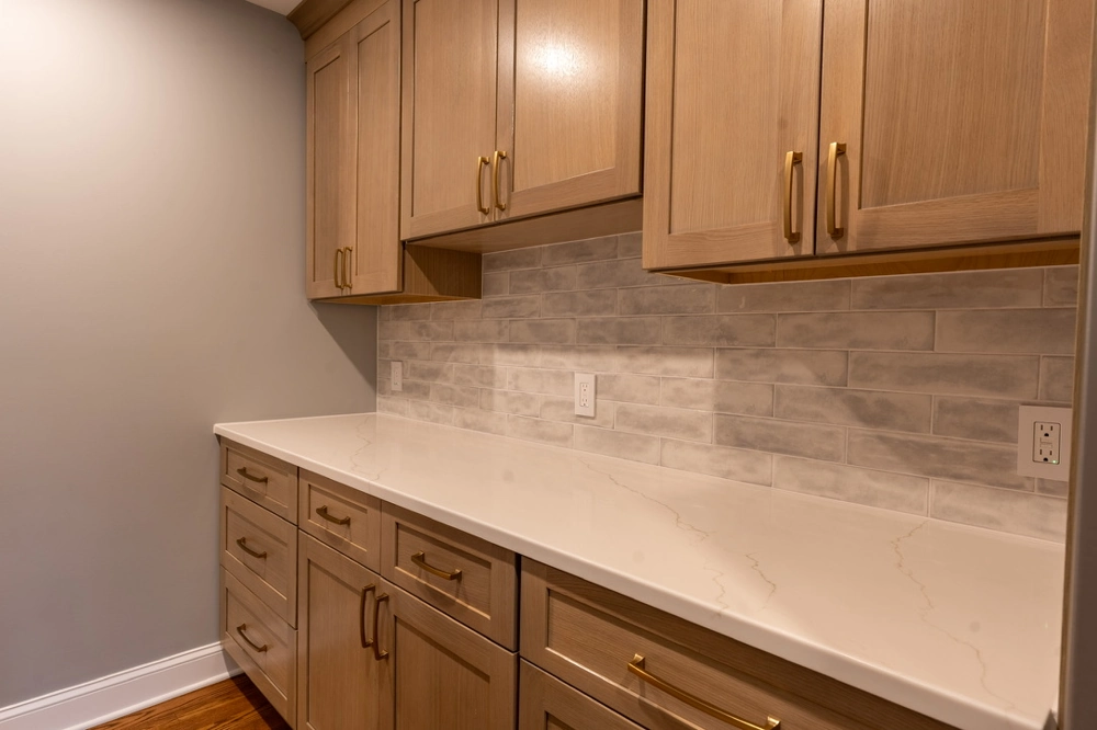 Backsplash Installation featuring marble-effect tile above quartz countertop and wood cabinets