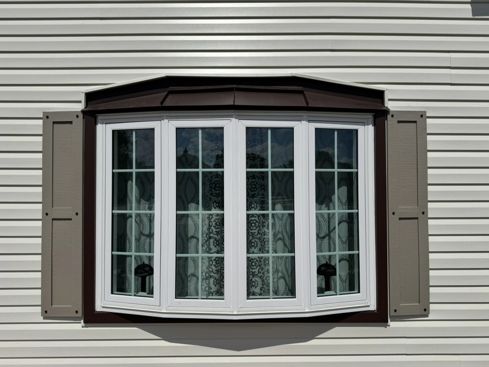Bay window installation with white vinyl frames and tan shutters on white siding