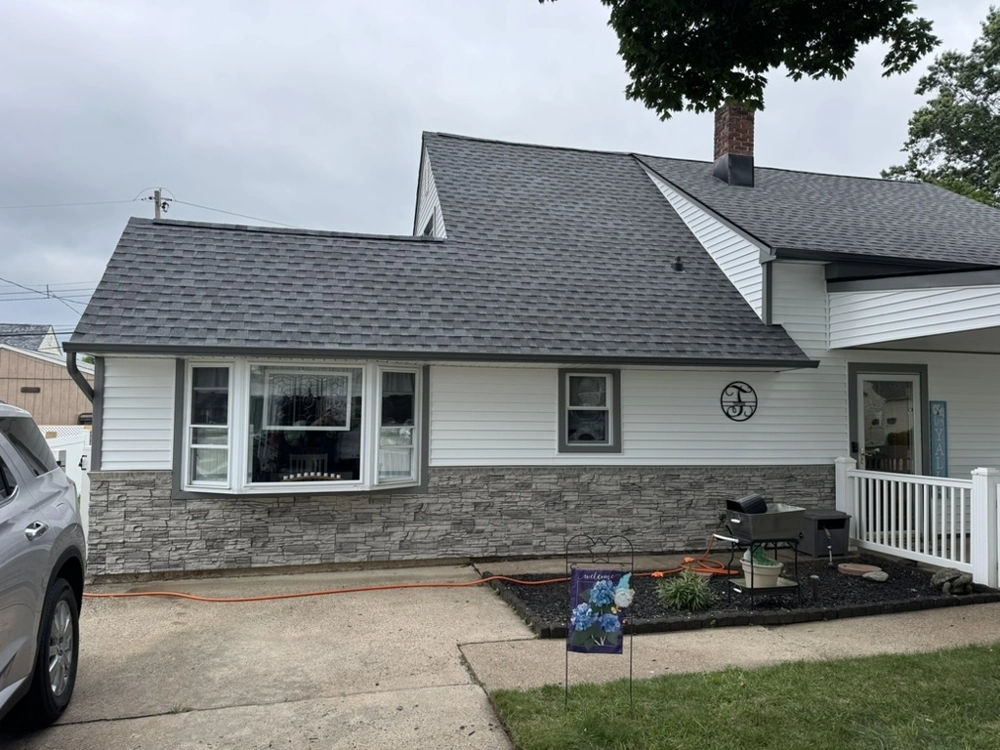 House exterior featuring vinyl siding installation, stone veneer base, shingle roofing, concrete driveway and garden bed