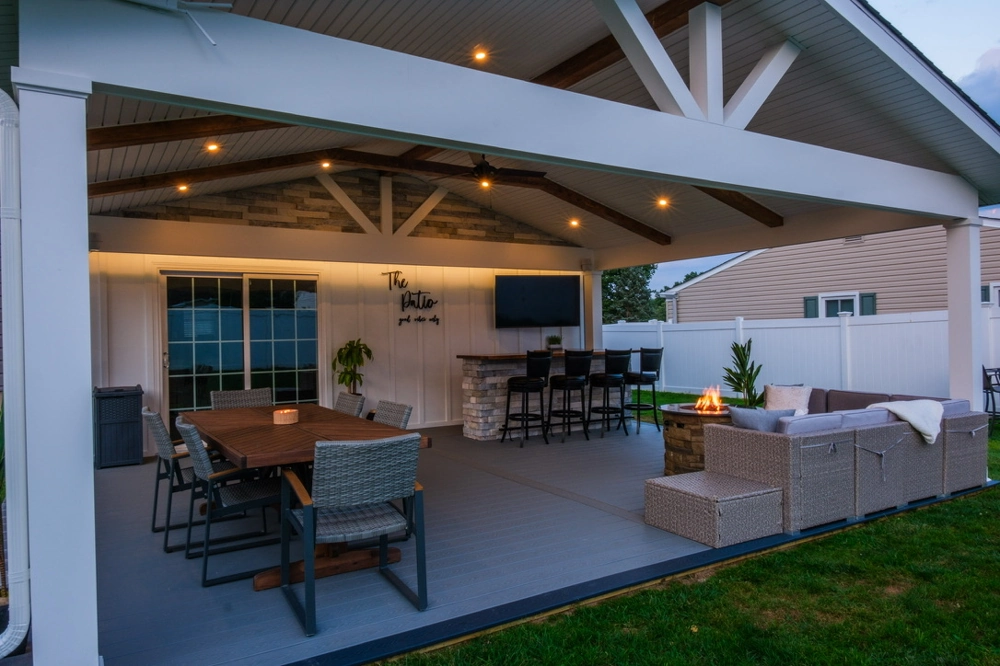Covered backyard deck with dining table, bar seating, sofa and fire pit under a vaulted pergola – Deck Installation