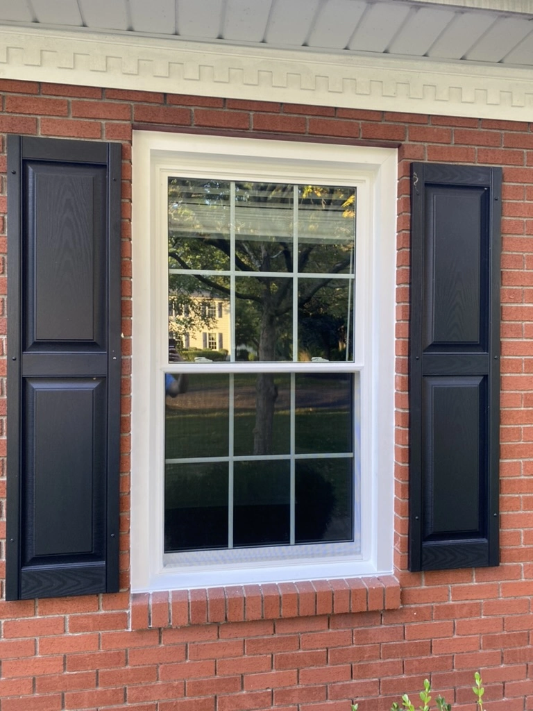 Red brick exterior with a newly installed white-framed grid window flanked by black shutters Window Installation