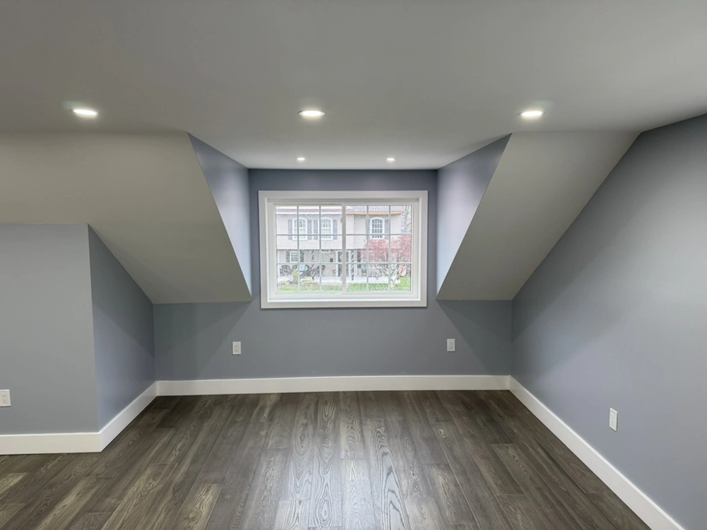 Finished basement room with gray painted walls, recessed lighting, white trim and dark hardwood flooring