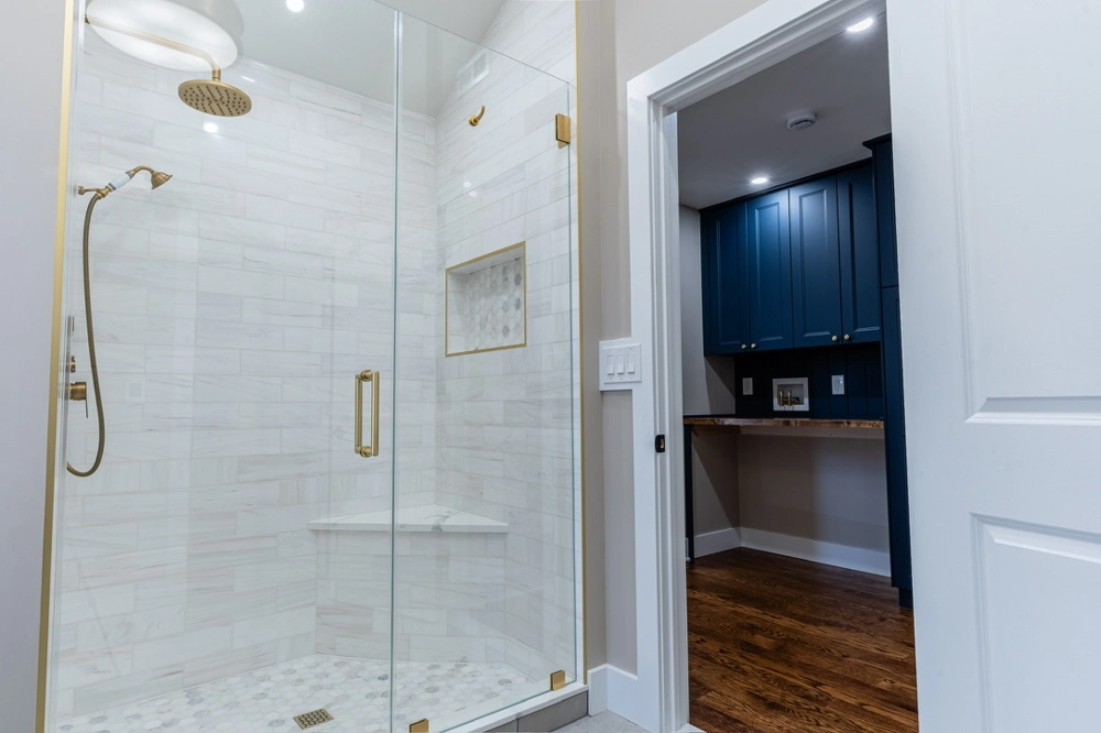Glass-enclosed shower with marble tile walls, brass fixtures and corner bench showcasing Tile Installation