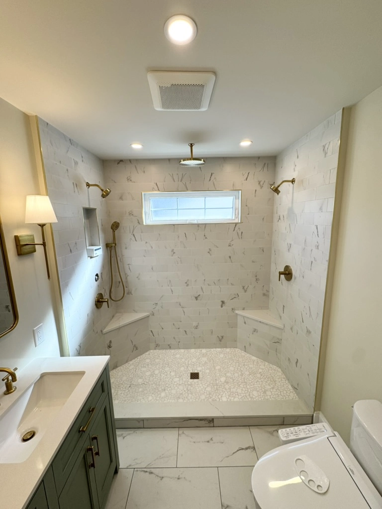 Custom tiled shower in Bathroom Renovation with marble-look walls, brass fixtures, built-in benches and overhead rain shower
