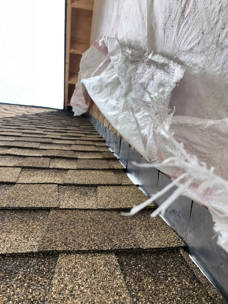Brown asphalt shingles and metal flashing at roof-wall junction during Shingle Roofing