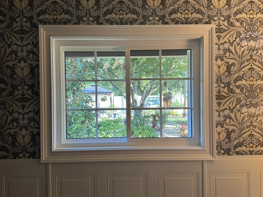 Interior of newly installed tilt and turn window with white trim and wainscoting overlooking garden Window Installation