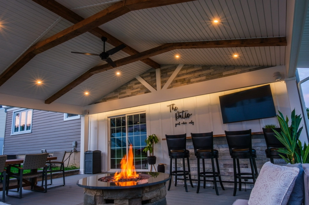 Covered patio showcasing Deck Installation with exposed wood beams, recessed lighting, fire pit and bar seating