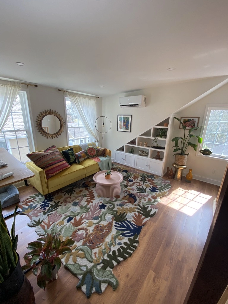 Bright living room with yellow sofa on new hardwood flooring, pink coffee table and built-in stair shelving showcasing Hardwood Flooring