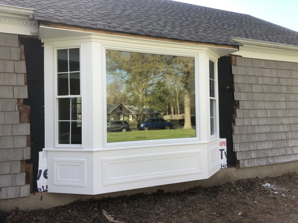 White bay window installed on house exterior amid removed siding during Window Installation