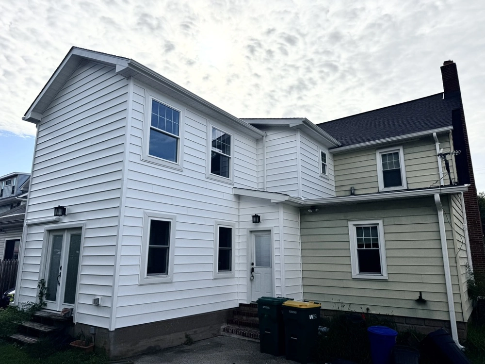 Two-story home extension with fresh white vinyl siding installation and new windows next to existing beige siding