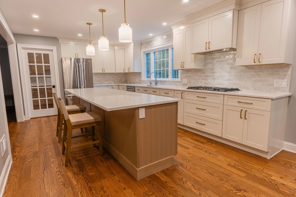Modern kitchen interior after Kitchen Remodeling with white cabinetry, central island, pendant lights, tile backsplash and hardwood flooring