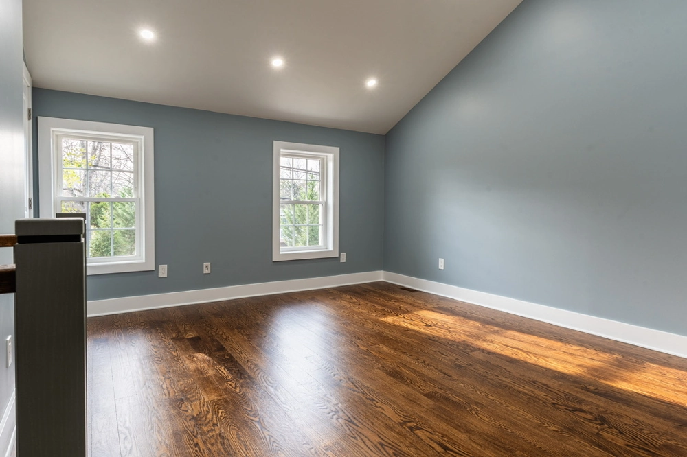 Empty room showcasing new Hardwood Flooring with fresh gray painted walls, white trim and recessed ceiling lights