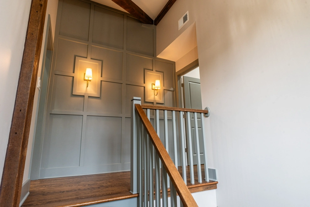 Second-floor landing with gray paneled accent wall, hardwood stairs, new railing and brass sconces Finish Carpentry