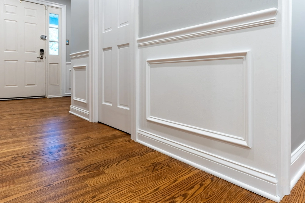Hallway with newly installed hardwood flooring and white baseboards beneath decorative wall panels