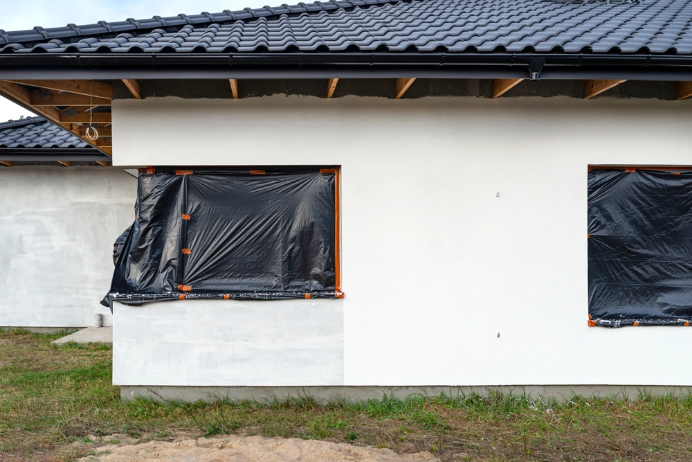 House exterior wall with windows masked by plastic sheeting in preparation for exterior painting