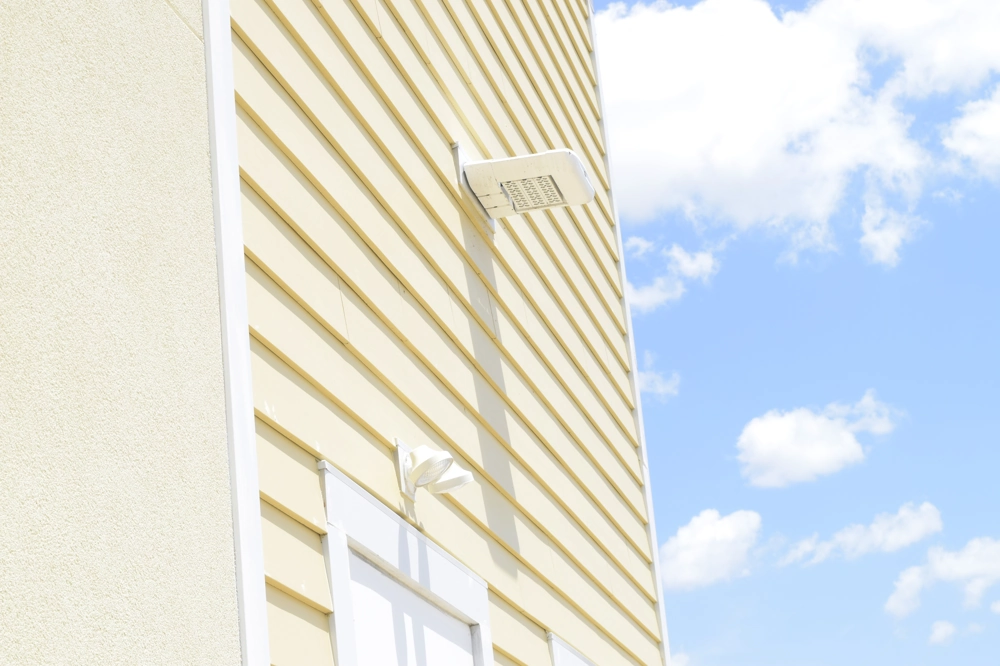 Yellow vinyl siding wall with white-trim window and exterior light fixture, example of Siding Installation