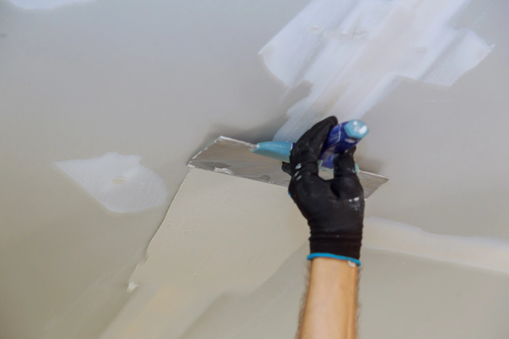 Gloved hand smoothing joint compound on a ceiling drywall panel Drywall Installation