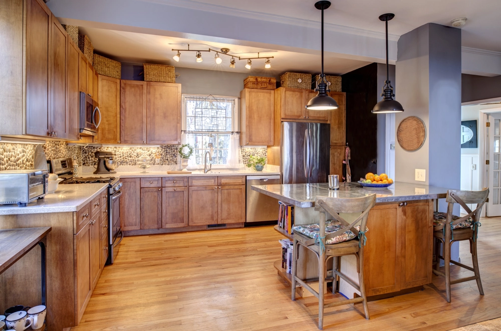 Open kitchen with custom wooden cabinets, stone backsplash, central island with bar stools and hardwood flooring reflecting kitchen remodeling