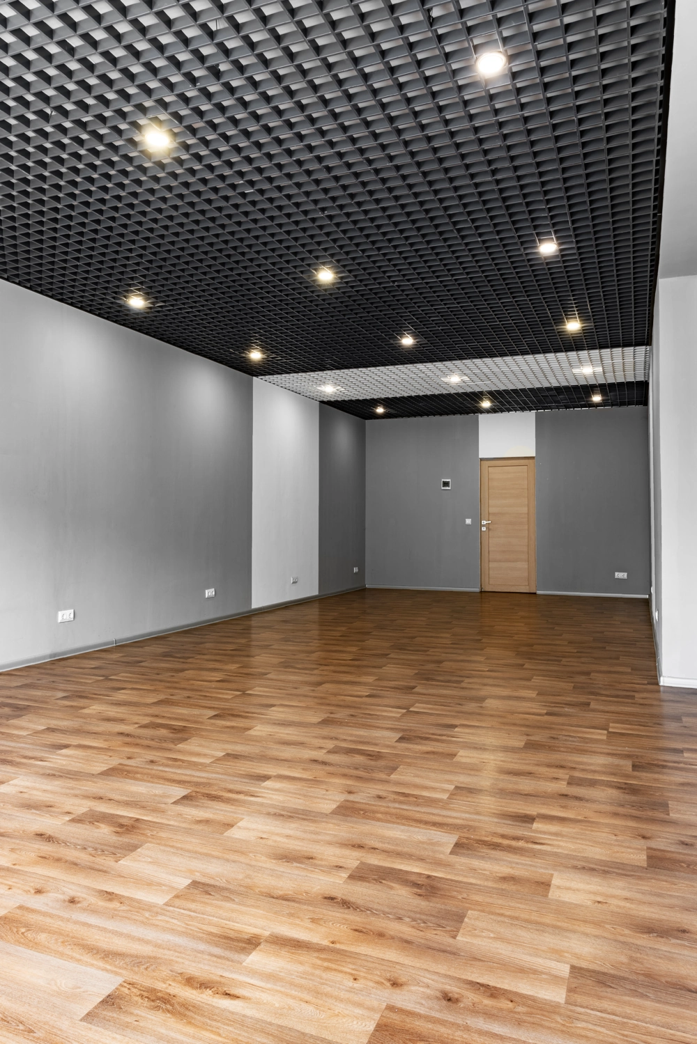 Empty room with freshly installed Hardwood Flooring and black Drop Ceiling grid with recessed lights