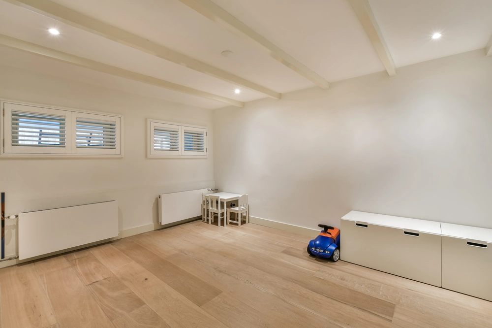 Finished basement with light hardwood flooring, recessed lighting, white walls and children's play area Basement Finishing