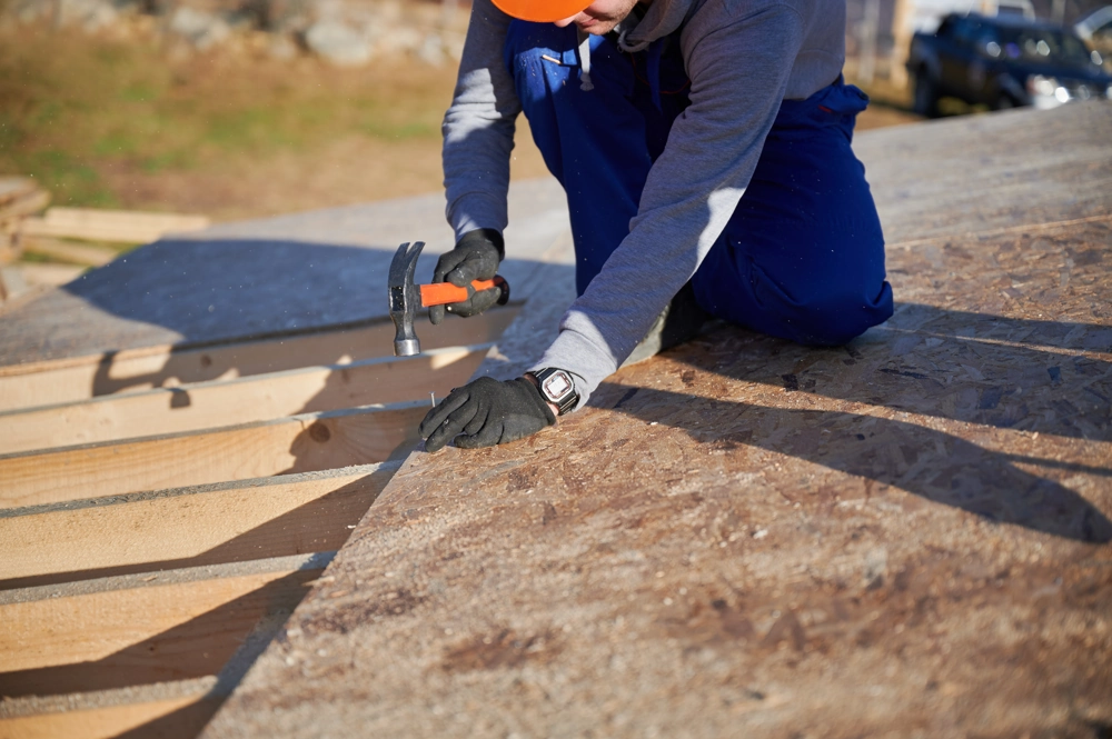 Construction worker installing roof sheathing with hammer on wooden roof frame – Roof Installation