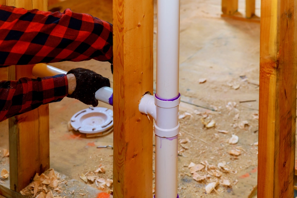 Worker installing PVC pipes inside wall studs for Plumbing service