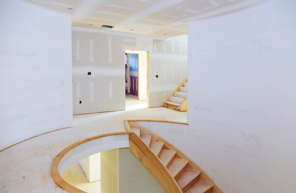 Unfinished home interior with new drywall, curved wooden staircase framing and open doorway during drywall installation