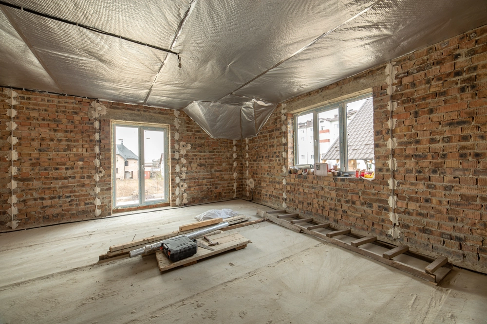 Home Renovation interior with exposed brick walls, foil ceiling insulation, new windows and ladder on floor
