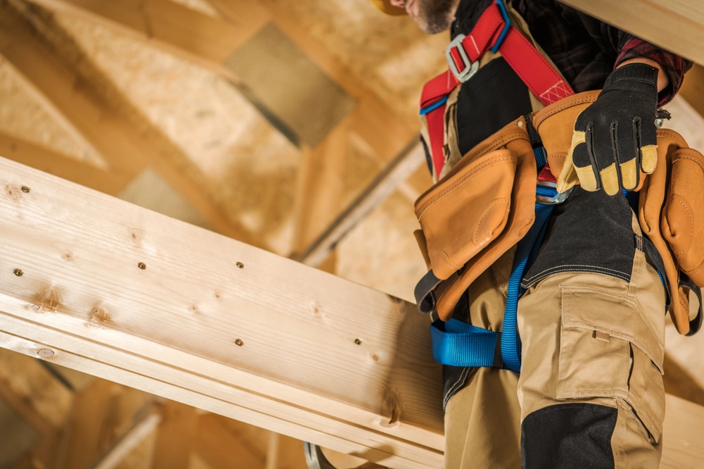 Construction worker in safety harness and tool belt installing wooden roof framing during Home Remodeling