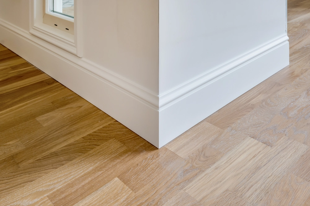 Baseboards Installation: white baseboards fitted along interior wall corner over hardwood flooring