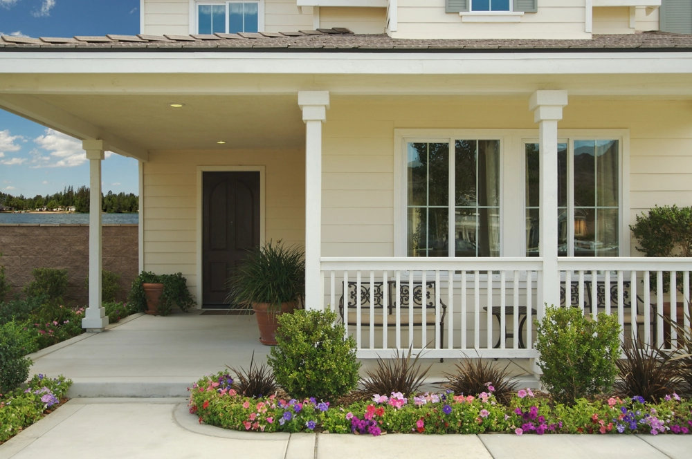 Front porch with new siding installation featuring white columns, railing, tilt and turn windows and colorful flower beds