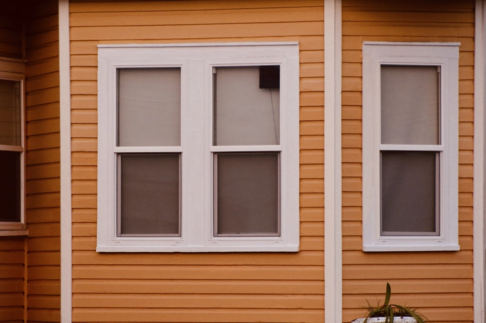 Three white-framed windows on tan vinyl siding exterior wall Window Installation