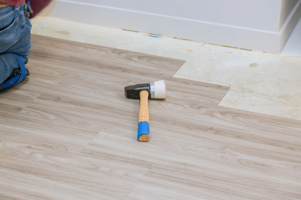 Worker fitting vinyl plank flooring with rubber mallet during Flooring Installation