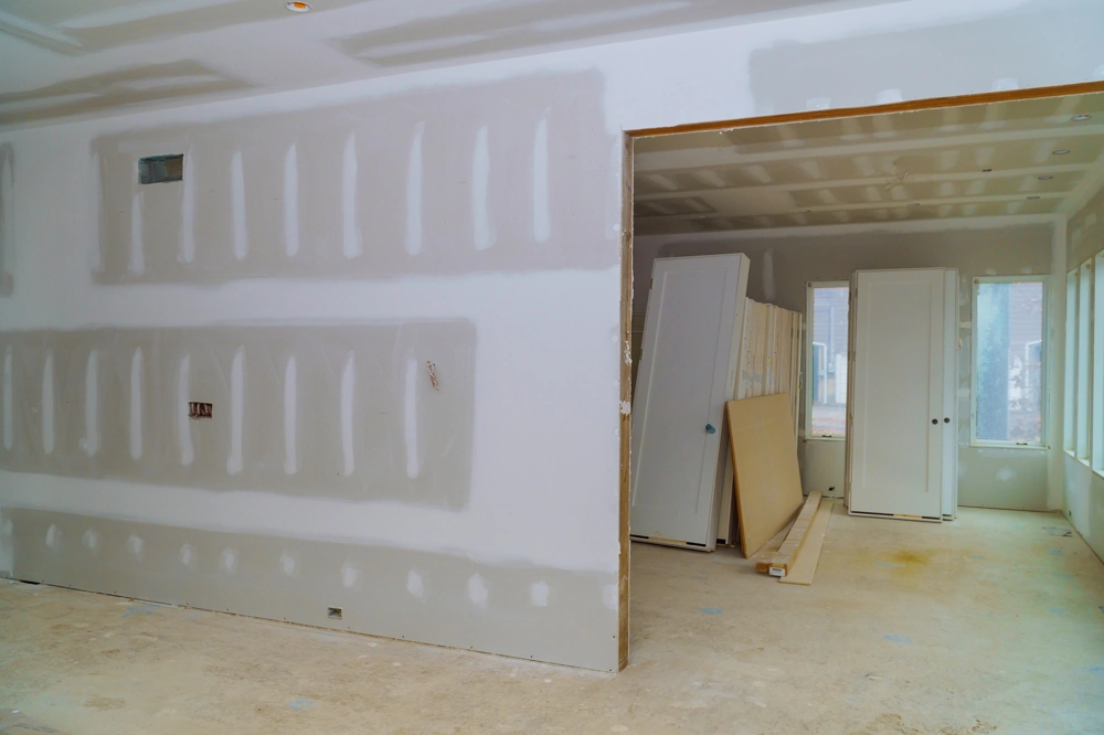 Drywall Installation: room interior with newly mounted drywall panels, taped seams, and construction materials