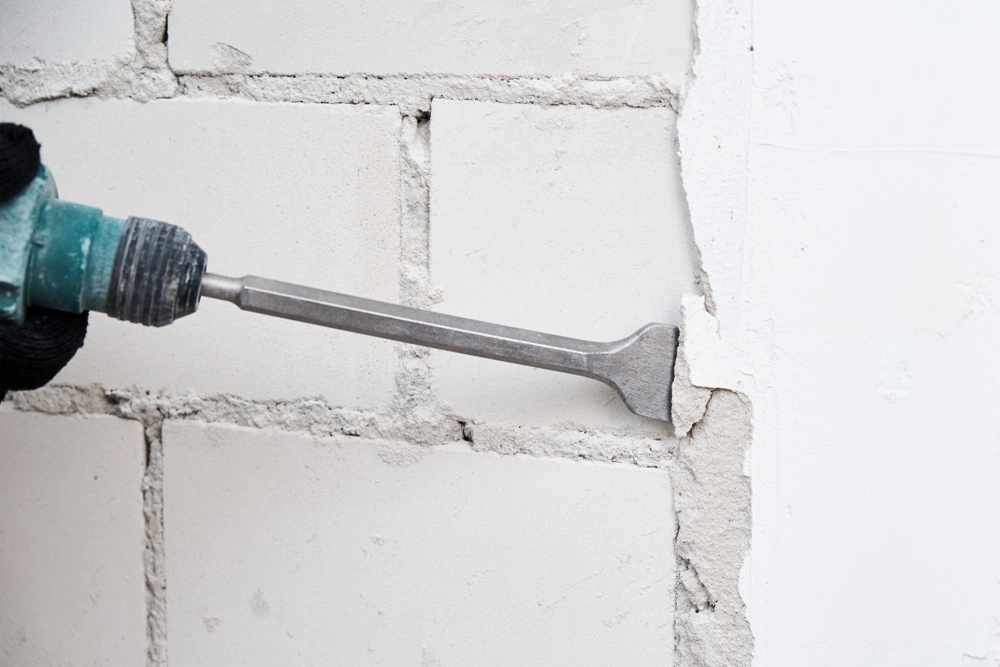 Handheld rotary hammer with chisel bit removing plaster from concrete block wall – Demolition