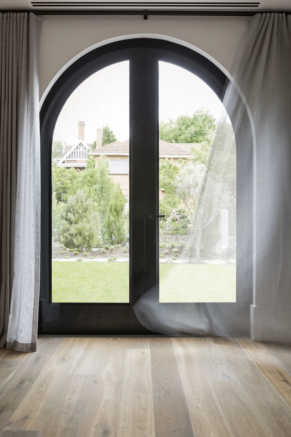 Arched double glass door with sheer curtains opening to garden over newly installed hardwood flooring