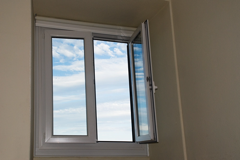 White outward-opening window in a neutral interior wall with sky view – Window Installation