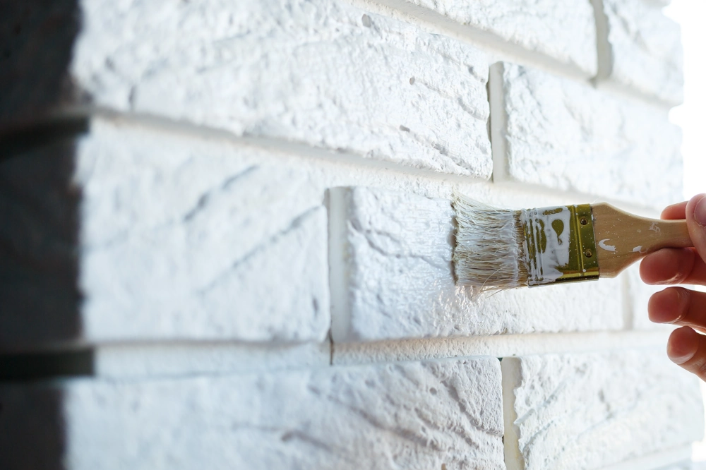 Hand applying white paint with a brush on brick wall – Interior Painting