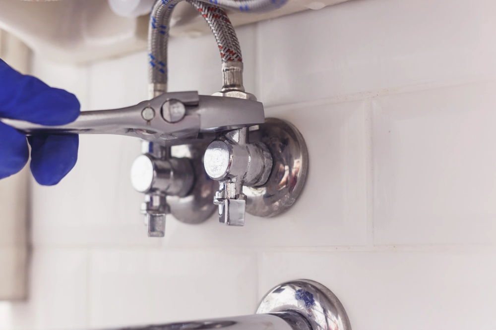 Plumbing: gloved hand using wrench to tighten water supply valve under sink