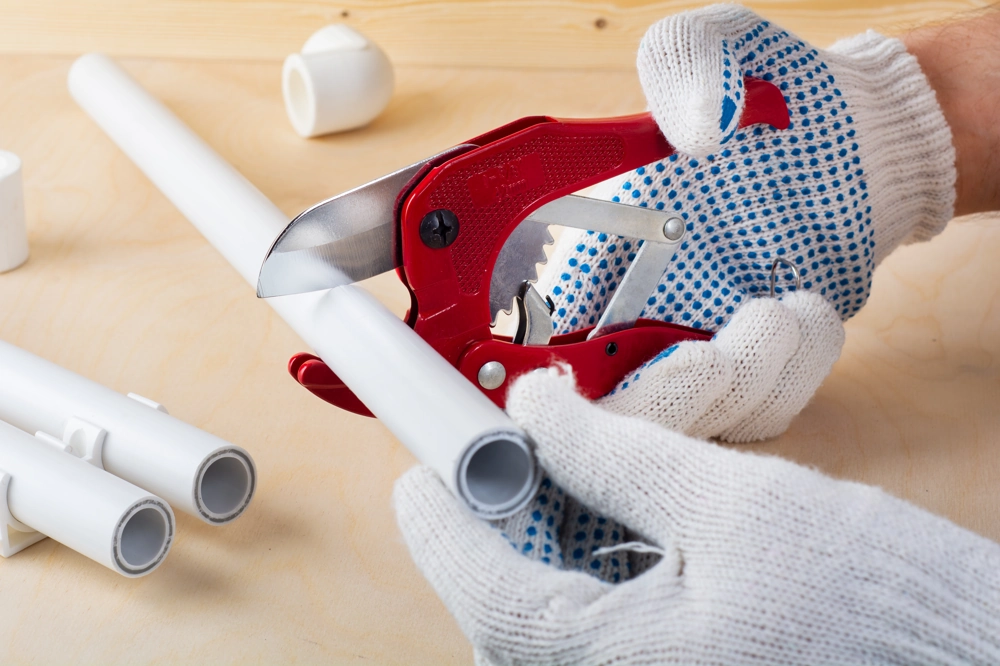 Manual cutting of PVC pipe with gloves and pipe cutter during Plumbing work