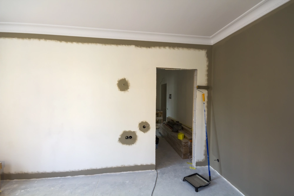 Interior Painting showing partially painted wall, paint roller, tray and patched electrical outlets