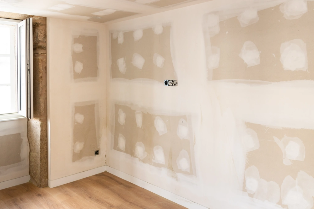 Corner of room with freshly installed drywall panels and taped seams over hardwood flooring
