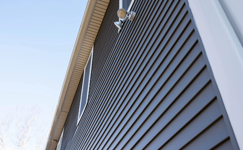 Close-up of dark vinyl siding and exterior light fixture near window opening