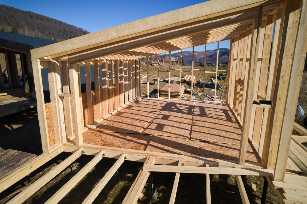 Wooden framing of new room addition with floor joists and wall studs on construction site Home Addition