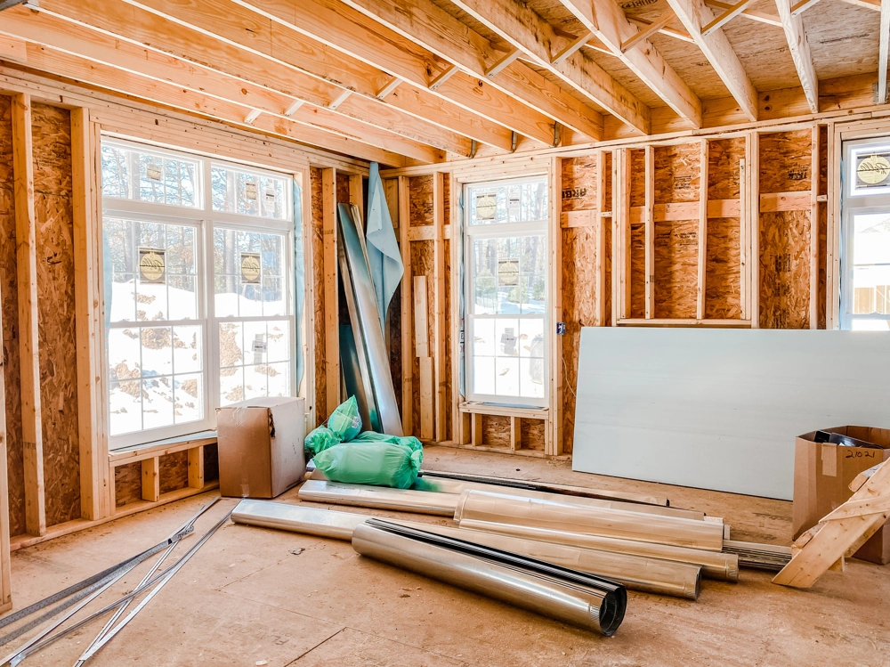 Interior room under renovation with exposed wooden studs, windows and stacked drywall panels ready for drywall installation