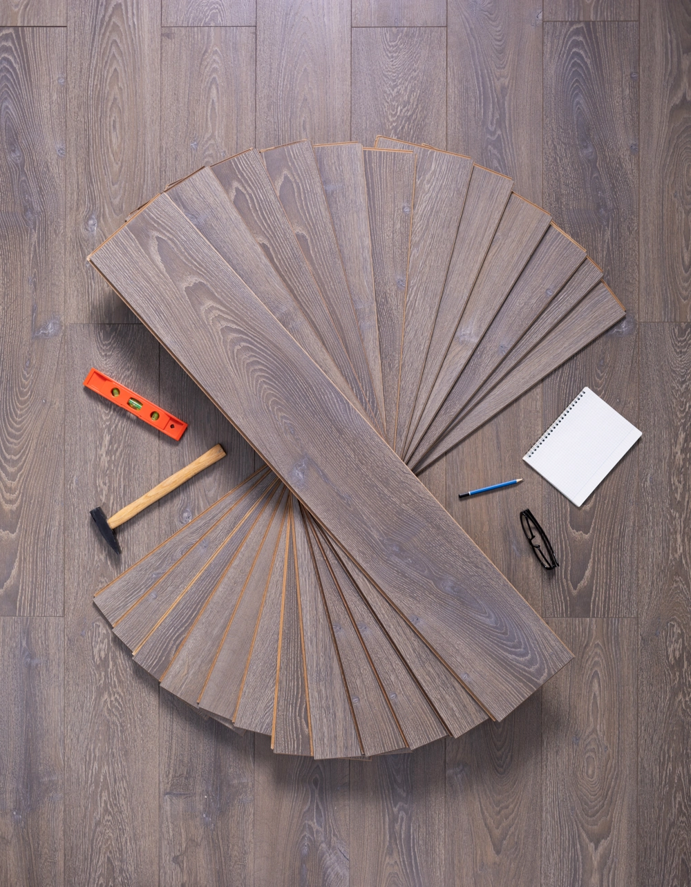 Spread wooden planks, hammer, level, notebook and glasses on floor ready for Hardwood Flooring